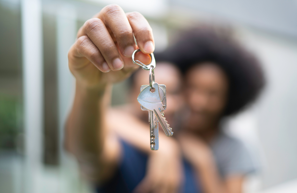 Young couple in front of a house, holding keys of their new home