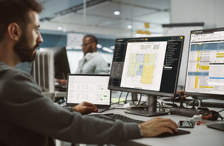 Construction estimating office: an enthusiastic estimator working on desktop computers and using ConstructBuy, TAKEOFF, and ESTIMATION simultaneously.