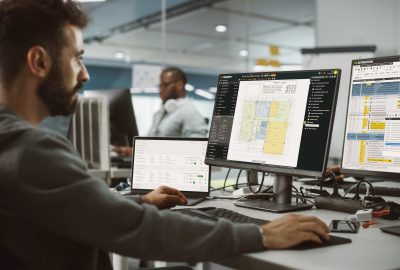 Construction estimating office: an enthusiastic estimator working on desktop computers and using ConstructBuy, TAKEOFF, and ESTIMATION simultaneously.